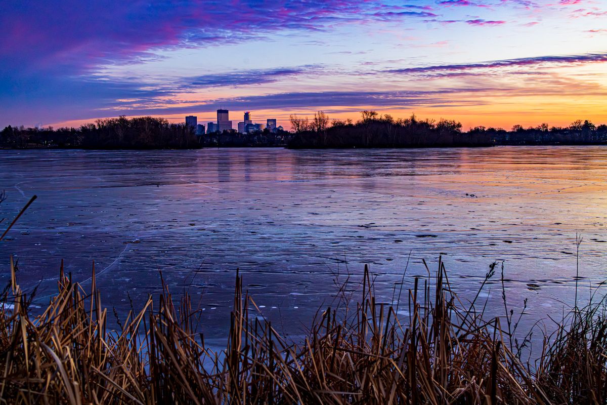 The Minneapolis skyline can be seen across an Icy Lake of the Isles during a colorful sunrise